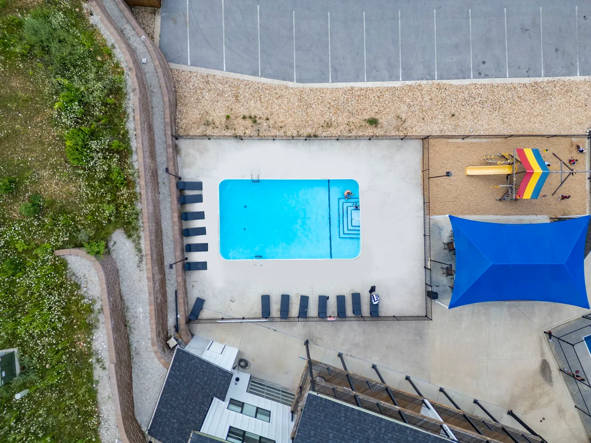 A playful and vibrant exterior view of the property’s swimming pool area, featuring sunlit lounge chairs, children’s playground equipment, and a shaded structure. Families can be seen enjoying the poolside, and children are playing, reinforcing a joyful, active environment for all ages.