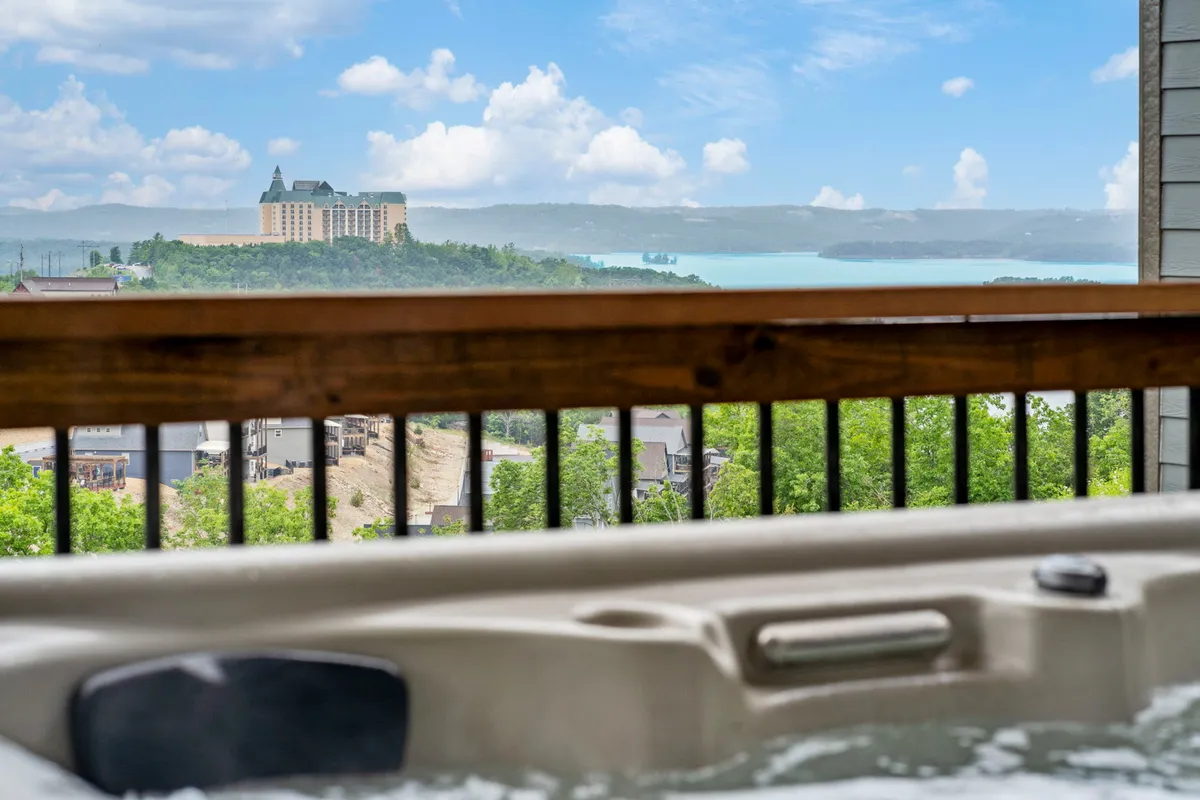 This exterior shot presents another perspective of a hot tub set on a lower patio, opening out to dramatic lake views and a broad, open sky. The scene is serene, with the lake shimmering in the background and space for quiet conversation or peaceful solitude.