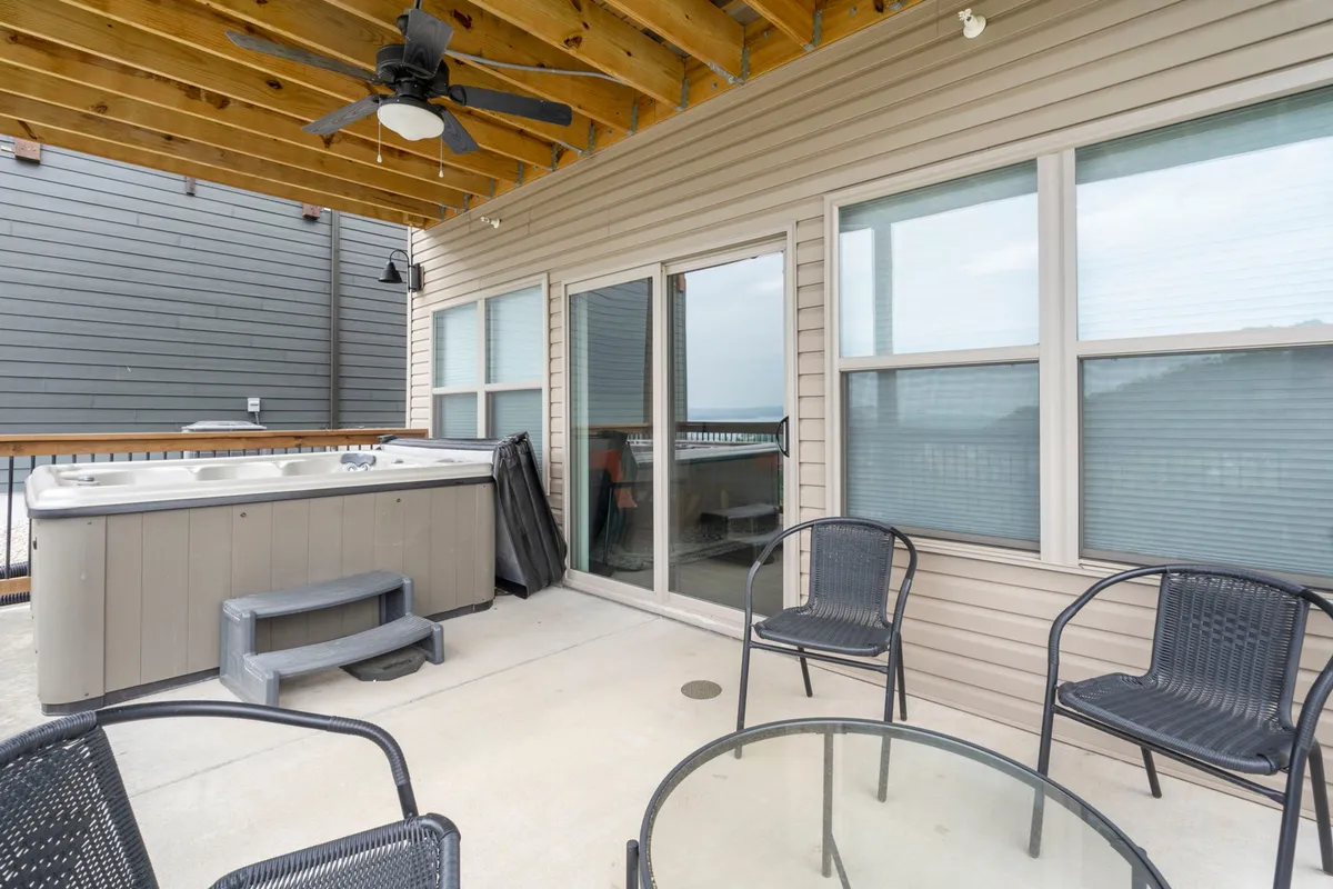 This exterior image features a luxurious hot tub on a private deck, paired with inviting outdoor seating and sliding glass doors leading back into the home. The setting is tranquil and offers a clear view of the surrounding natural landscape, evoking a sense of peaceful retreat and relaxation.