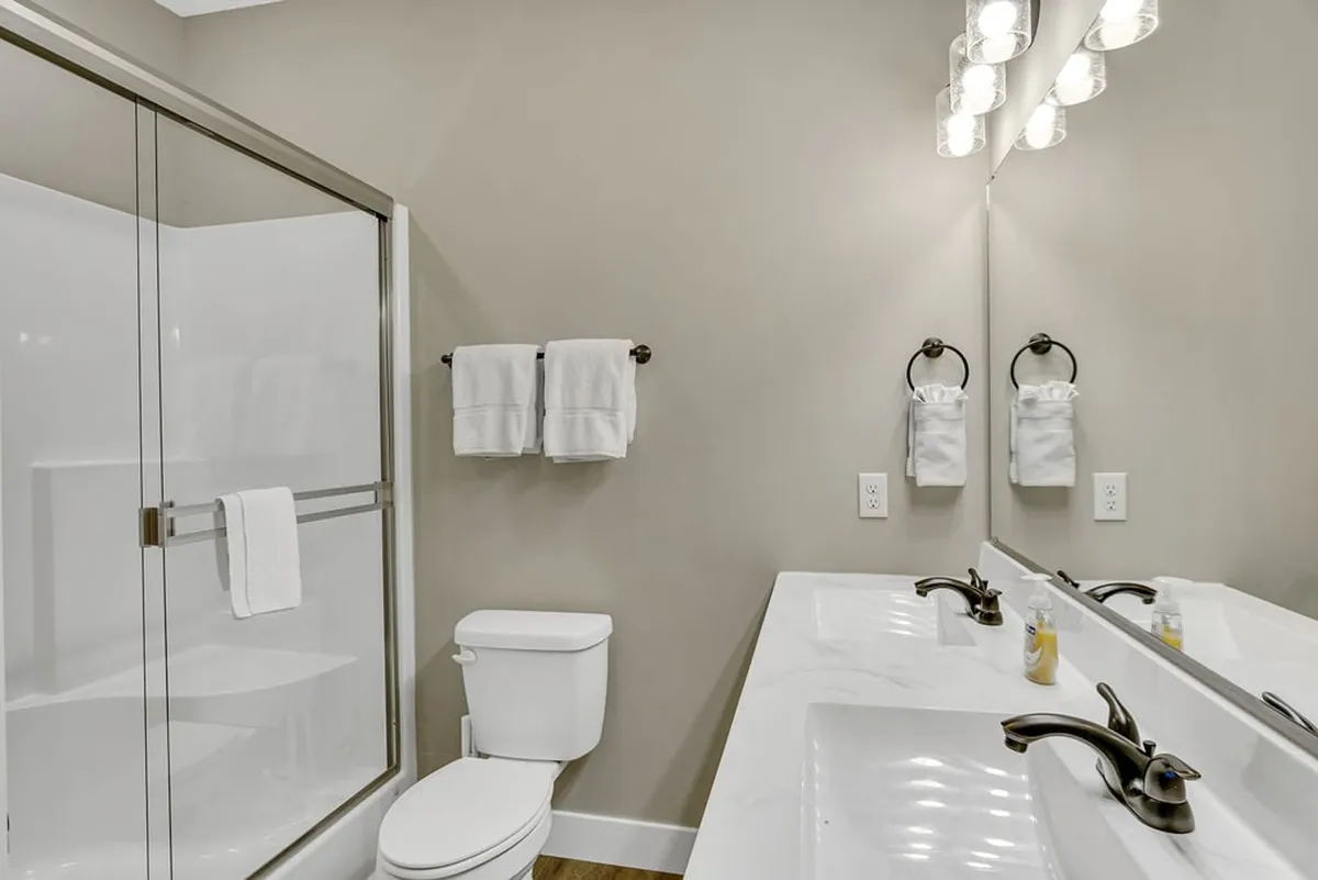 A modern ensuite bathroom with double vanity sinks, a glass shower enclosure, and sleek lighting fixtures. The clean lines and organized space highlight both functionality and luxury.