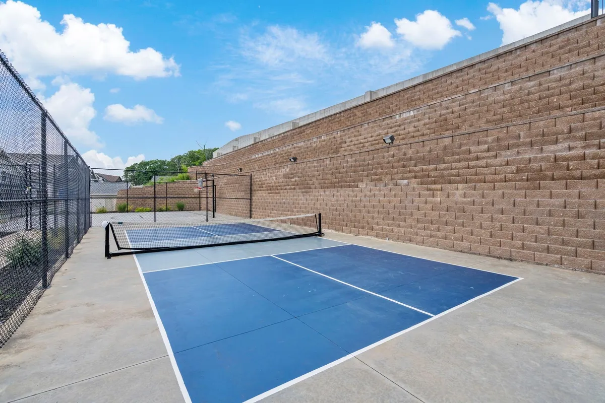 A bright, energetic view of the community pickleball court, bordered by a chain-link fence and set against a textured wall, suggesting a space for exercise and social gatherings.