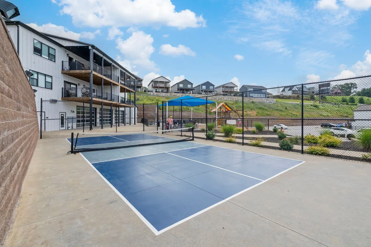 This exterior shot features tennis courts, a playground area bustling with children, and balconies overlooking green hills—showcasing multiple amenities and the property’s vibrant outdoor setting.