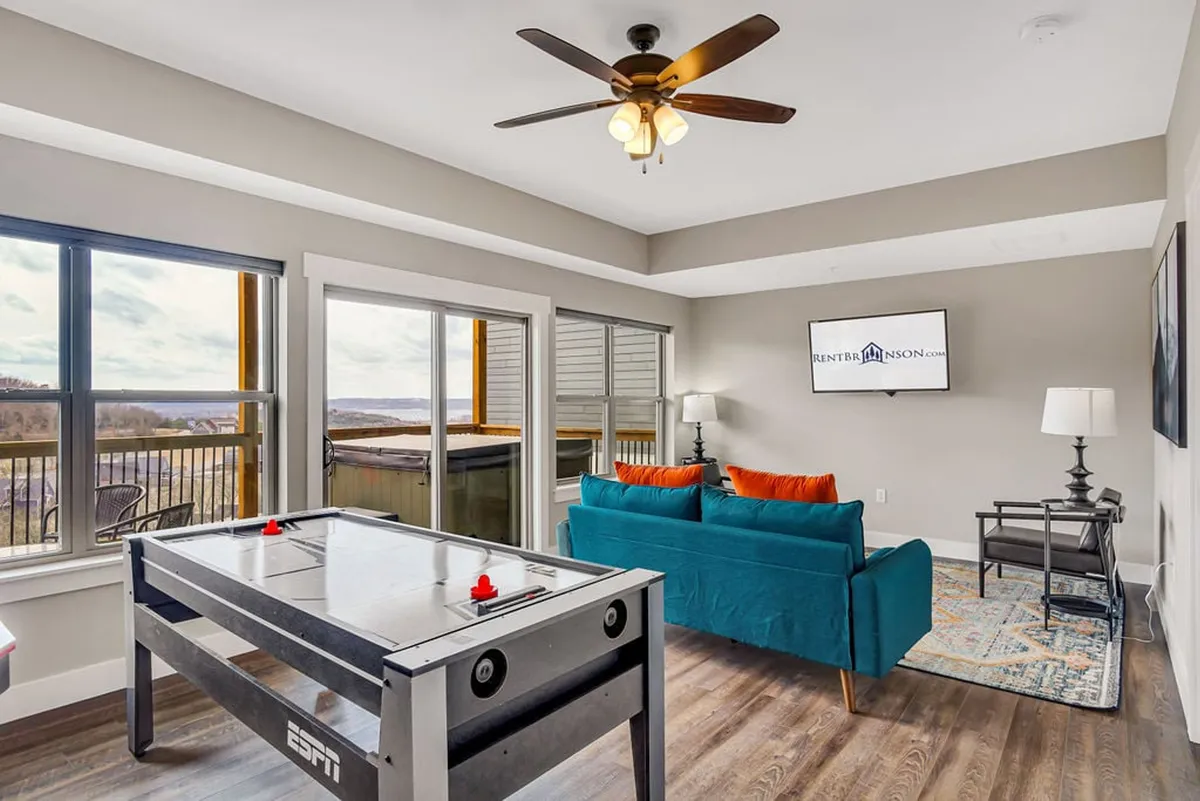 This view highlights an air hockey table positioned in front of a comfortable sofa and a large TV, with expansive windows letting in natural light. The setup is ideal for both active play and cozy movie nights.