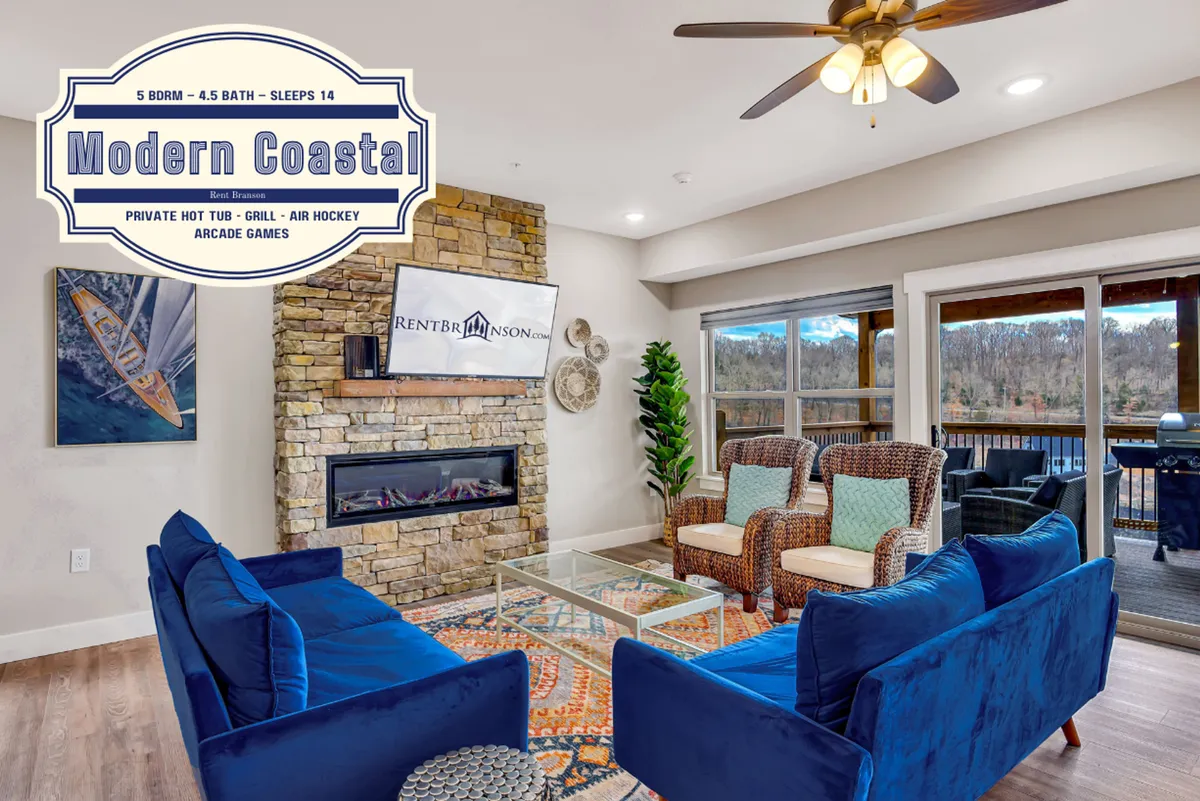 A bright, cheerful living room with blue sofas, a colorful area rug, a stone fireplace, and large windows letting in plenty of sunlight. The furniture is arranged invitingly, suggesting a space meant for gathering and relaxation.